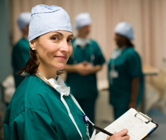 A woman in green scrubs holding a clipboard.